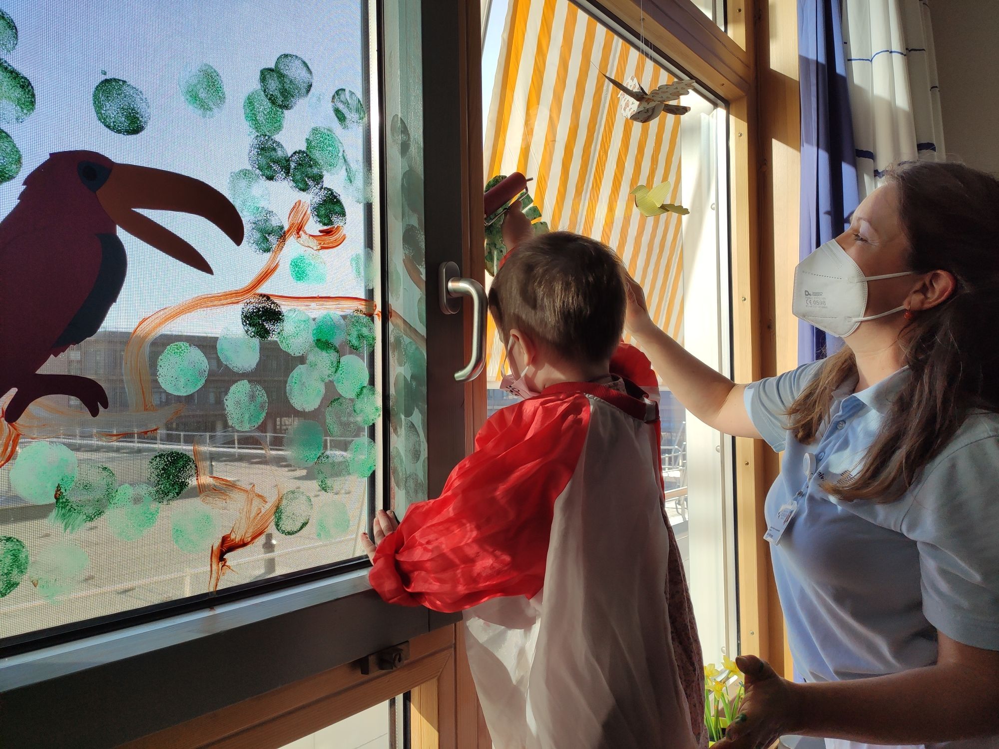 krebskrankes Kind malt mit Betreuerin an Fenster